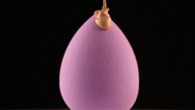 Makeup liquid foundation pouring on make-up blender sponge, closeup. Foundation beauty facial cosmetics, tool for perfect make up. Dripping bb cream or concealer, over black background. Slow motion