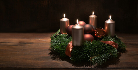 Fourth Advent wreath with copper colored candles and Christmas decoration baubles on a rustic wooden table against a dark brown background, panoramic format, copy space, selected focus