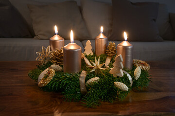 Advent wreath with four golden lit candles and natural winter decoration on a wooden coffee table...