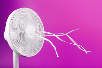 The electric fan is white with pink ribbons fluttering in the wind on a pink background.