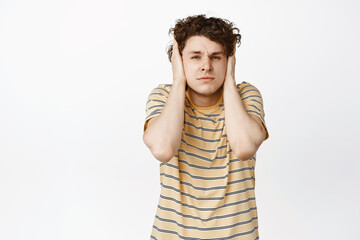 Distressed curly guy shut his ears and looking troubled, having probem, standing annoyed against...