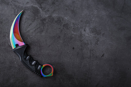 Kerambit dagger with a rainbow-colored blade on a dark textured background.