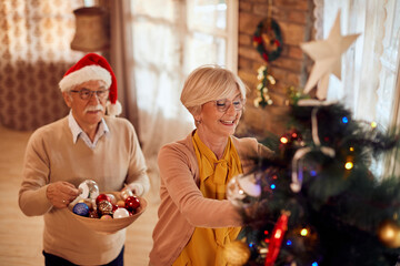 Happy mature couple decorating Christmas tree in the living room.