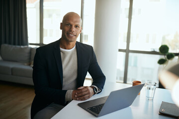 Portrait of black businessman using laptop at his office and looking at camera.