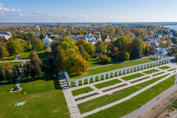 Panoramic aerial view of the Gostiny Dvor Arcade in Veliky Novgorod, autumn treetops on a sunny day. Remaining ruins of a medieval market. Monument to the heroes.