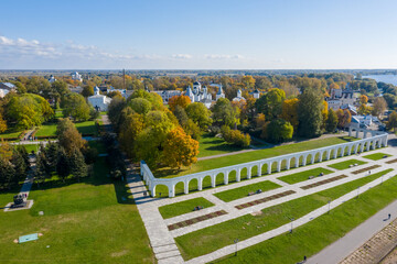 Panoramic aerial view of the Gostiny Dvor Arcade in Veliky Novgorod, autumn treetops on a sunny day. Remaining ruins of a medieval market. Monument to the heroes.