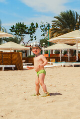 A small child runs along the beach of the Red Sea and makes faces. Umbrellas and sun beds on the shore of Safaga, Egypt.