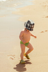 A small child runs along the beach of the Red Sea and makes faces. Safaga Coast, Egypt.