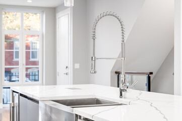 A kitchen sink detail shot with a chrome faucet, stainless steel apron sink, and white granite...