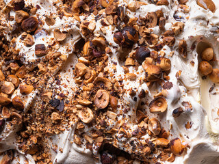 Frozen Hazelnut flavour gelato - full frame detail. Close up of a white creamy surface texture of Ice cream covered with pieces of nuts.