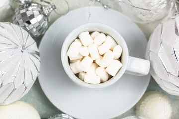 A cup of coffee with marshmallows on white tray and garlands, led lights. Christmas still life