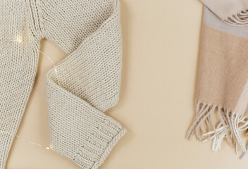 Women fashion winter clothes and accessories. Female look with knitted sweater, pullover, scarf, garlands on beige pastel background.  