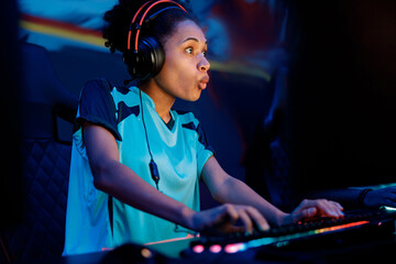 Young female esports player wearing wired headset surprised with game while playing online...