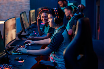 Side view of focused Asian man wearing headphones playing online video games while participating in esports tournament in gaming club