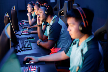 Team of four professional cybersport gamers wearing headphones playing online video games while participating in esports tournament in gaming club © Yaroslav Astakhov