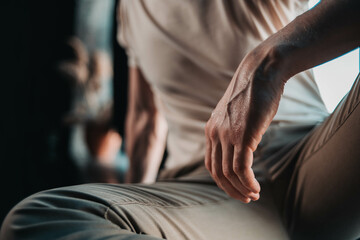  a man's hand close-up, a man in a light white T-shirt sits against the background of a window in brown trousers, a close-up of a hand, masculinity in details