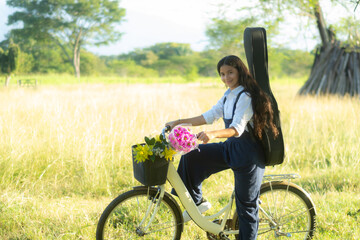 Adorable smiling young girl on a bicycle with a guitar on her back in the field
