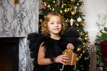 portrait of little girl with Christmas present in her hands near Christmas trees with lights. Merry Christmas and Happy Holidays