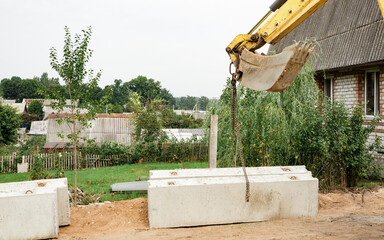Obraz premium Wheel loader. Excavator install the foundation blocks into a trench. Retaining wall building. Construction site. Workers manage installing. 