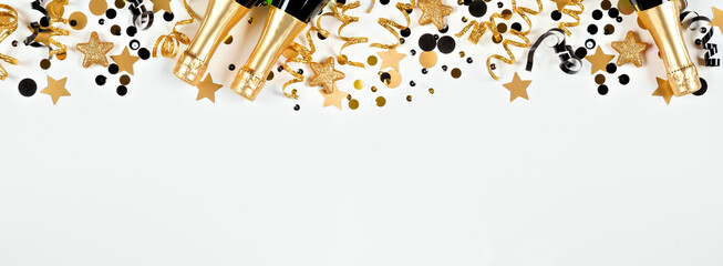New Years Eve top border of gold and black confetti, streamers and champagne. Overhead view over a...