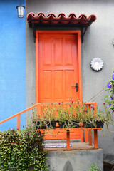 beautiful rustic orange door with flower vases and blue wall, passionate, romantic