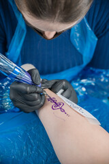 Close up of young female tattoo artist works making an unalome piece on a girl's leg using a sketch inside a tatto studio.