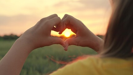 Happy girl making a heart shape with fingers. The light of the summer spring sun is on my hands. Travel, relax in nature. The girl molded a love heart out of her palms. The concept of a healthy heart