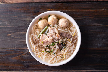 Rice noodles soup with pork and pork ball in a bowl on wooden background, Thai noodles soup, Table top view