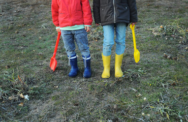 A little boy and girl in rubber boots are walking through the forest and holding shovels. Autumn forest, tourism.
