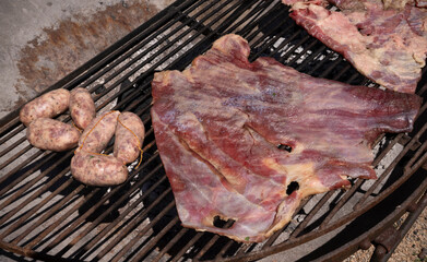Cooking red meat. Closeup view of pork meat, matambre, and pork sausages, chorizos, in the grill. 