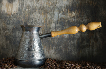 A turk with a wooden handle and coffee beans on a gray-brown background.

