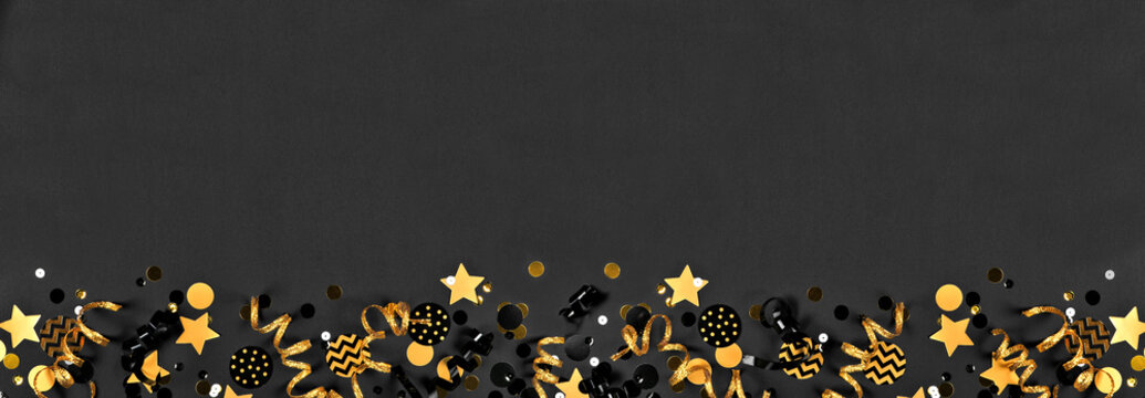 New Years party bottom border with glittery black and gold streamers and  confetti. Top down view on a black background. Stock Photo