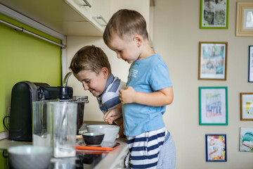 Two cheerful male children cooking homemade baking dessert together mixing ingredients for dough