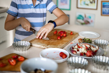 Cute boy slicing fresh berry strawberry on wooden board use knife cooking summer dessert at kitchen