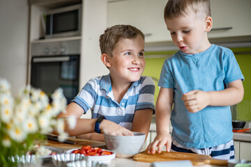 Funny brother male kids rejoicing having fun cooking summer dessert with fruits and berries