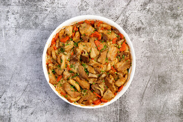 Oven baked pork belly with rice and vegetables in a white baking dish on a dark grey background. Top view, flat lay