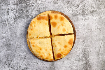 Traditional ossetian sliced pie with potatoes and curd on a round wooden cutting board on a dark grey background. Top view, flat lay