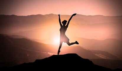 Young Happy Girl Jumps For Joy On The Top of Mountain Peak Above Clouds At Sunset. Free Success Woman and Freedom Concept 
