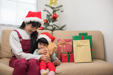 Obraz na płótnie Canvas Asian family Mother giving the teddy bear to child. Happy moment Mom and son in christmas festival. They dressing christmas theme with decorative pile gift box on sofa. Giving present each other.