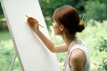 an artist in nature draws on an easel with a pencil
