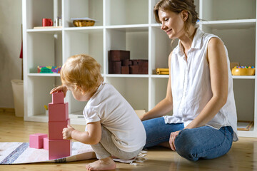 Young mother and little baby assembling pink cube Maria Montessori ecological materials