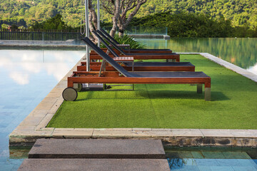 Side pool outdoor wooden day bed in a modern luxury resort with a nice clear sky, big mountain and pool reflection in a background.