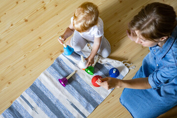 Young mother and little toddler playing childish colorful hand bells music sound at home