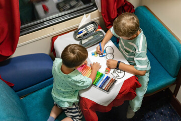 Funny little brothers travel by train riding at comfortable railway carriage drawing picture