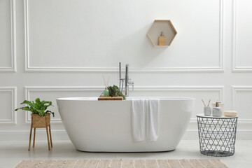 Modern ceramic bathtub and green plants near white wall in room