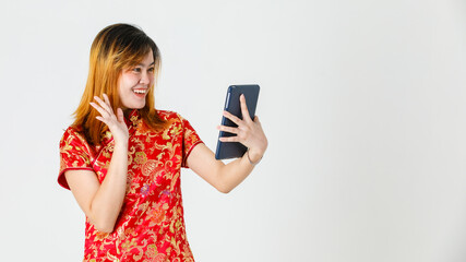 Studio shot of millennial Asian young teen female model in beautiful red gold Chinese traditional cheongsam qipao shirt stand holding touchscreen tablet video call greeting say hi on white background