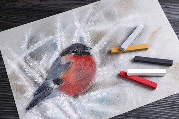 Colorful chalk pastels and beautiful painting of bullfinch on black wooden table, top view - Powered by Adobe