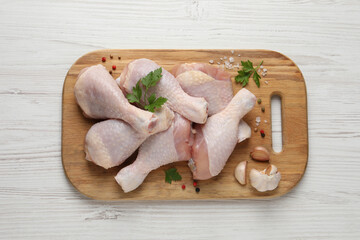 Fototapeta premium Raw chicken drumsticks with parsley, spices and garlic on white wooden table, top view