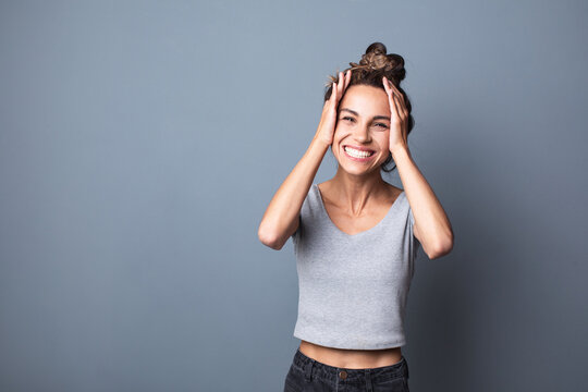 Happy excited charming woman holding her head on gray studio background.