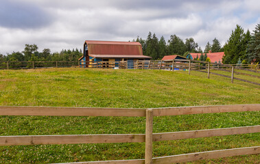 A wooden fence leading up to a big red barn. Rustic red barn in rural area in British Columbia.
